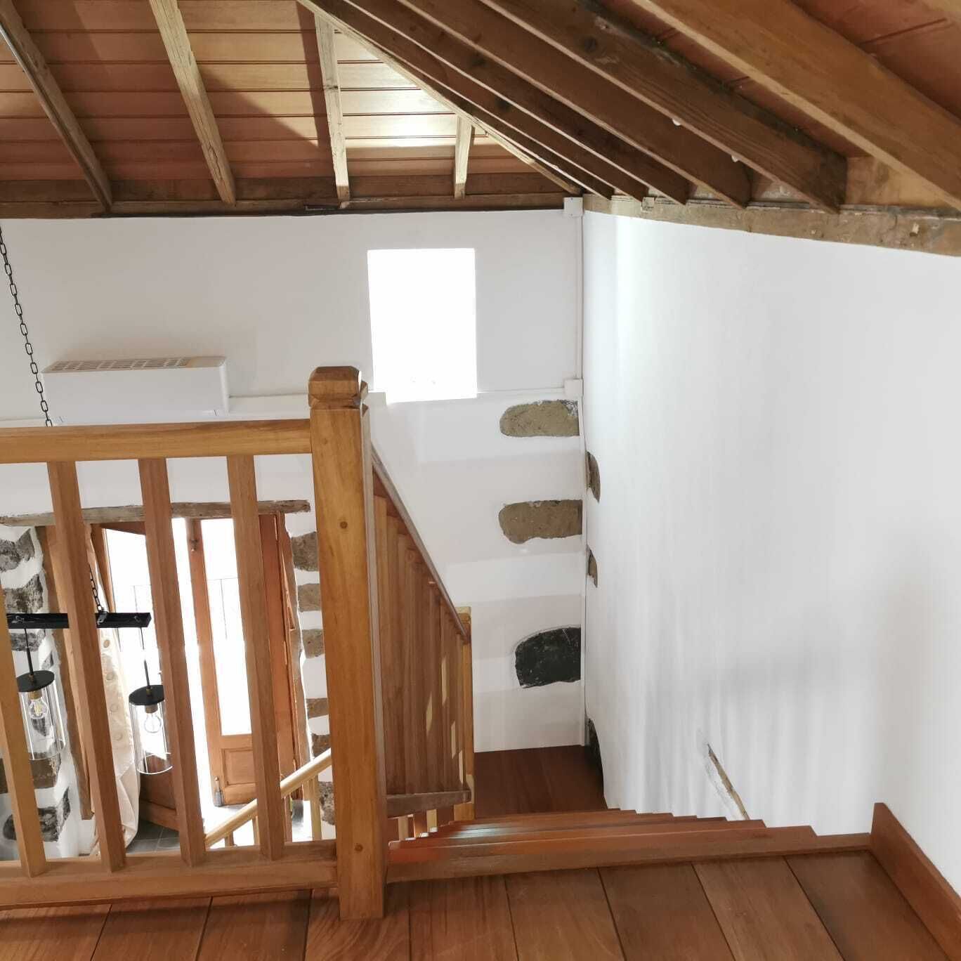 A wooden staircase leading to an upper level with a white wall and a small window.