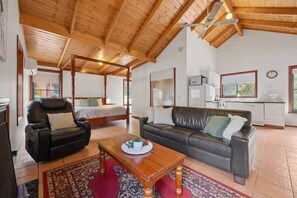 A spacious room with a wooden ceiling, a bed, a sofa, a coffee table, and a kitchen area.