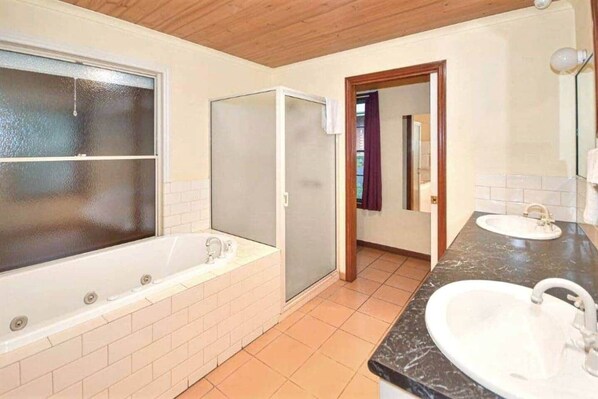 A bathroom with a bathtub, two sinks, and a shower area.