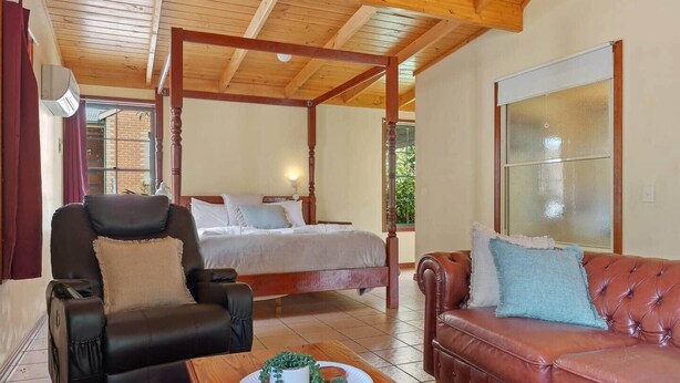 Ein Zimmer mit einem Bett, einem Ledersessel, einer Couch und einer Holzbalkendecke.