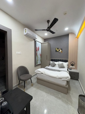 A modern bedroom with a bed, a chair, a table, and an air conditioning unit.