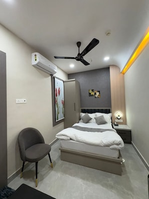 A modern bedroom with a bed, a ceiling fan, an air conditioner, a nightstand, and a chair.