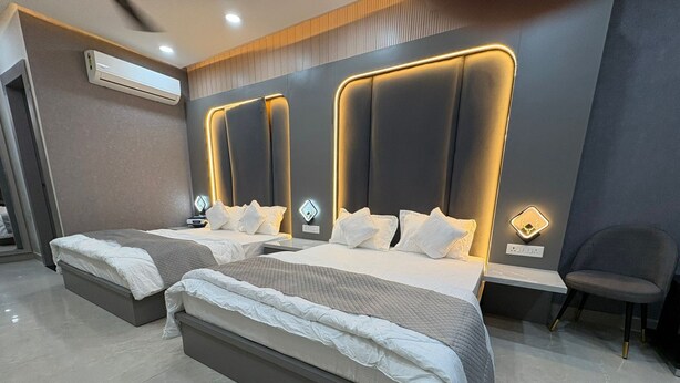 A modern hotel room with two beds, a seating area, and a wall-mounted air conditioner. - Hotel R J Heights (Fatehpur)