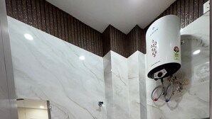 A modern bathroom with a marble wall, a toilet, a sink, and a shower with a water heater. - Hotel R J Heights (Fatehpur)