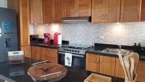 Une cuisine moderne avec des meubles en bois, un réfrigérateur en acier inoxydable, une machine à café rouge, une cuisinière à gaz et une planche à découper en bois.