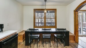 Un comedor con una mesa y sillas de madera, una ventana que da a árboles y un ventilador de techo.