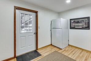 Una habitación con una puerta blanca, un refrigerador blanco, un cuadro en la pared y piso de madera.