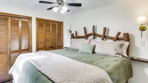 Un dormitorio con cama, cabecera de madera, ventilador de techo y mesita de noche con lámpara.