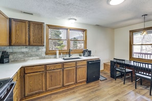 A kitchen with wooden cabinets, a dishwasher, a sink, and a dining area with chairs and a table. - ‘Raley's Retreat’ w/ Hot Tub: 2 Mi to Dtwn Boone! (Boone)