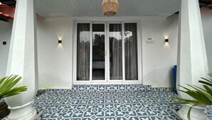Eine überdachte Veranda mit gemusterten Fliesen, weißen Säulen und einer hängenden Leuchte.
