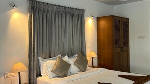 Ein ordentlich bezogenes Bett mit Kissen, ein Holzschrank und zwei Nachttischlampen in einem Zimmer mit gemustertem Boden und weißer Decke.