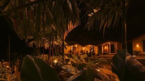 Ein tropisches Resort bei Nacht mit beleuchtetem Eingang, üppiger Vegetation und ruhiger Atmosphäre.