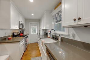 Una cocina moderna con armarios blancos, electrodomésticos de acero inoxidable y un ventanal grande.