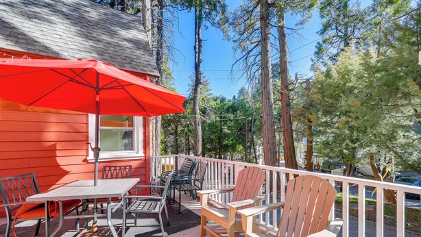 Une terrasse en bois avec un parasol rouge, des chaises en métal et une table.