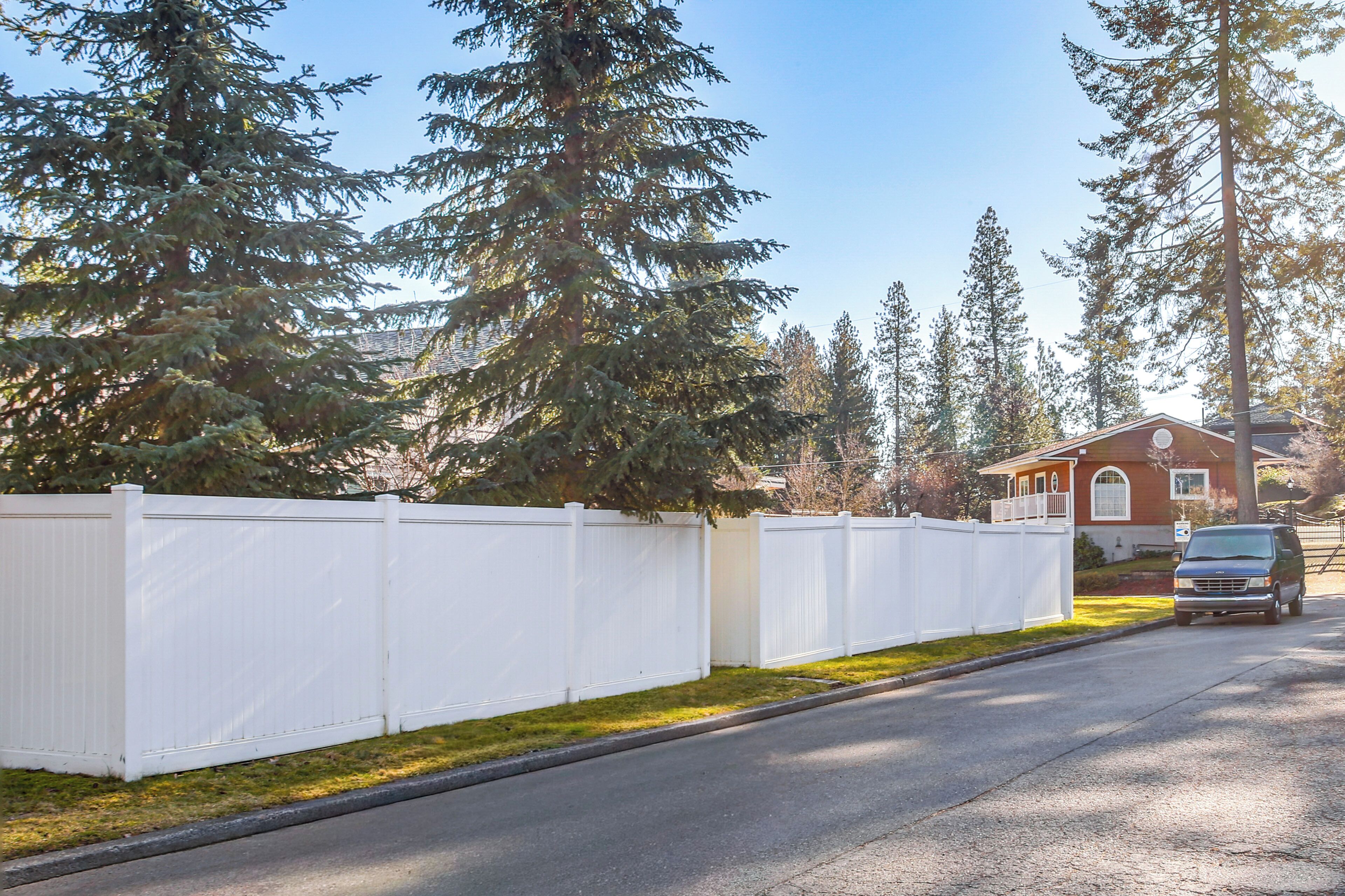 Une rue résidentielle bordée d’une clôture blanche, une maison avec un toit rouge et une voiture garée.