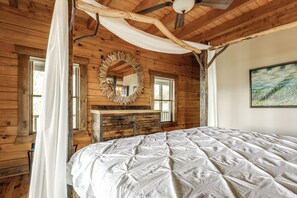 A wooden cabin bedroom with a bed, a dresser, a mirror, and a painting on the wall. - Game Room + Deck: Spacious Spruce Pine Retreat! (Spruce Pine)