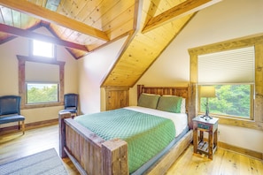 Un dormitorio con techo de madera, una cama con colcha verde, dos sillas, una mesita de noche y una ventana con vistas.