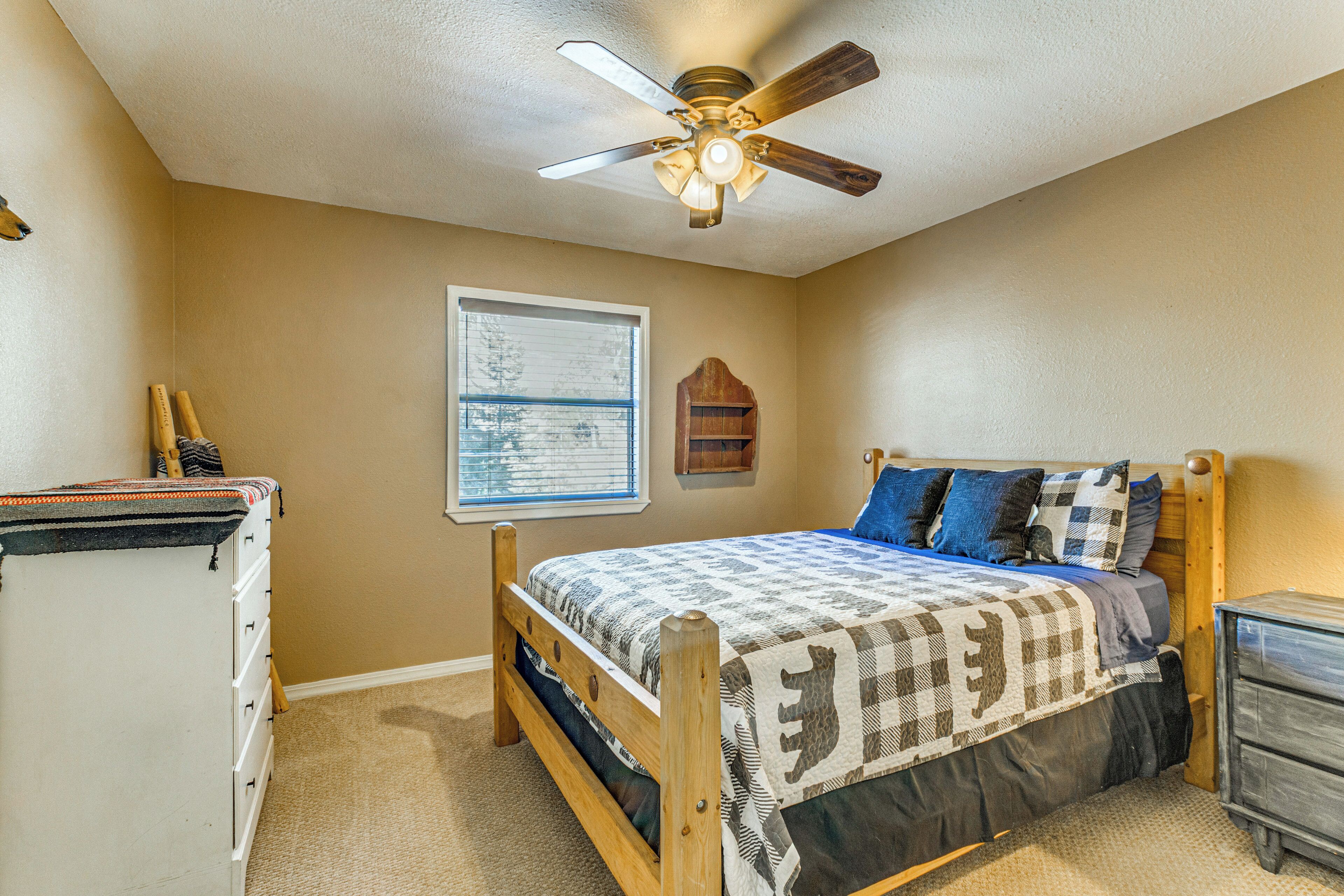 A bedroom with a bed, a ceiling fan, a window, a dresser, and a nightstand.