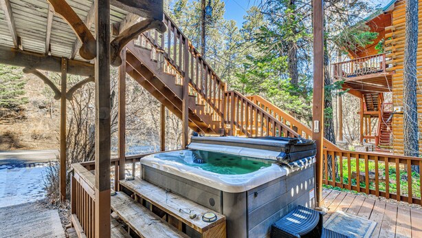 Ein Whirlpool auf einer Holzterrasse mit einer Holztreppe zu einem überdachten Bereich.