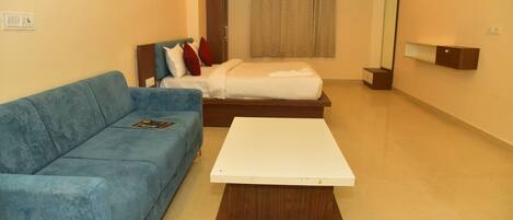 A room with a blue sofa, a bed with a white mattress, and a wooden table.