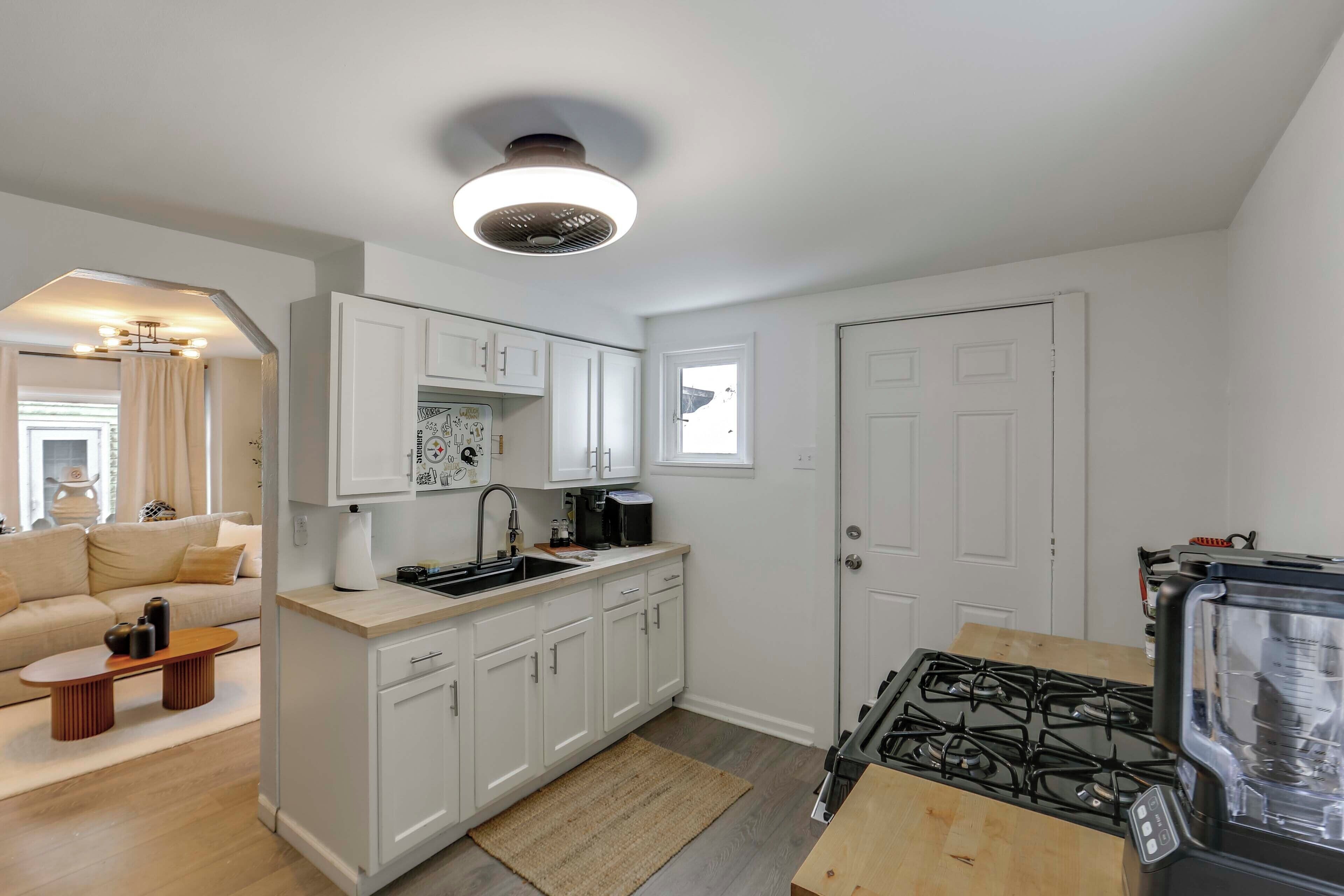 A modern kitchen with white cabinets, a gas stove, a coffee machine, and a small dining area with a table and chairs.