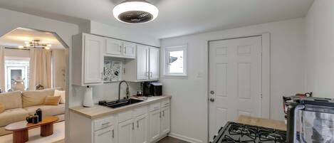 A modern kitchen with white cabinets, a gas stove, a coffee machine, and a small dining area with a table and chairs.