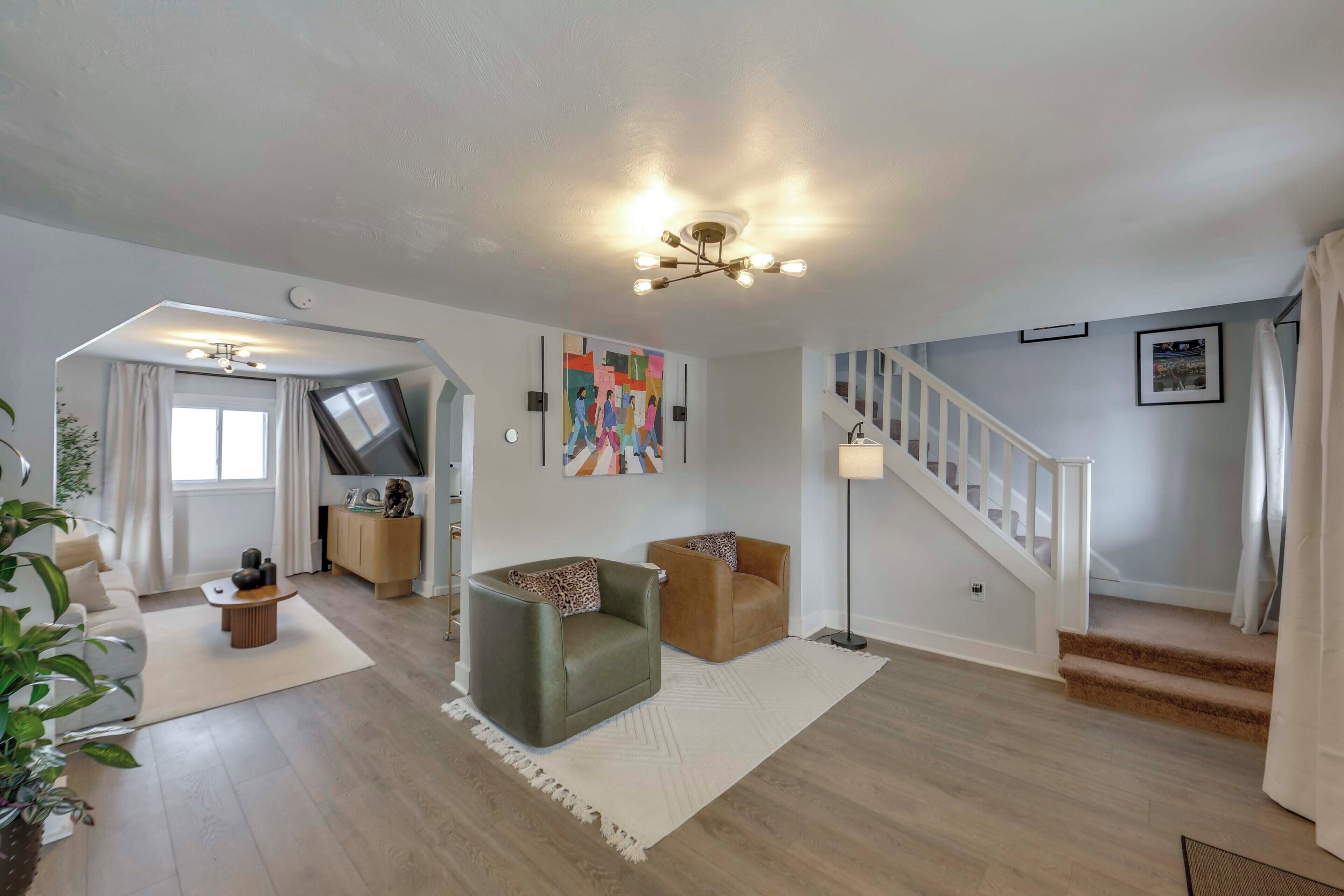 A modern living room with a sofa, two armchairs, a coffee table, a staircase, and a ceiling light fixture.