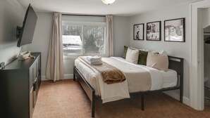 Un dormitori amb un llit, una televisió sobre una cómoda, una finestra amb cortines i tres quadres a la paret.