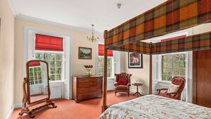Ein Schlafzimmer mit Himmelbett, Kommode, Stuhl und Spiegel.