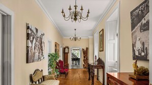 Ein Flur mit Holzboden, einer Kristalllüster, einem roten Sessel, einem Holzschrank und Wandbildern.