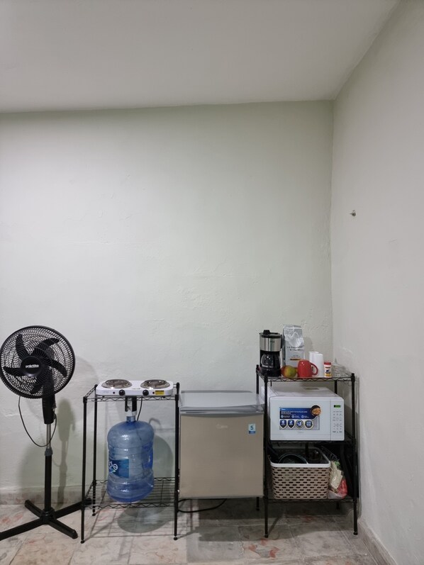 A small kitchenette with a water dispenser, a coffee maker, and a microwave on a metal shelf.