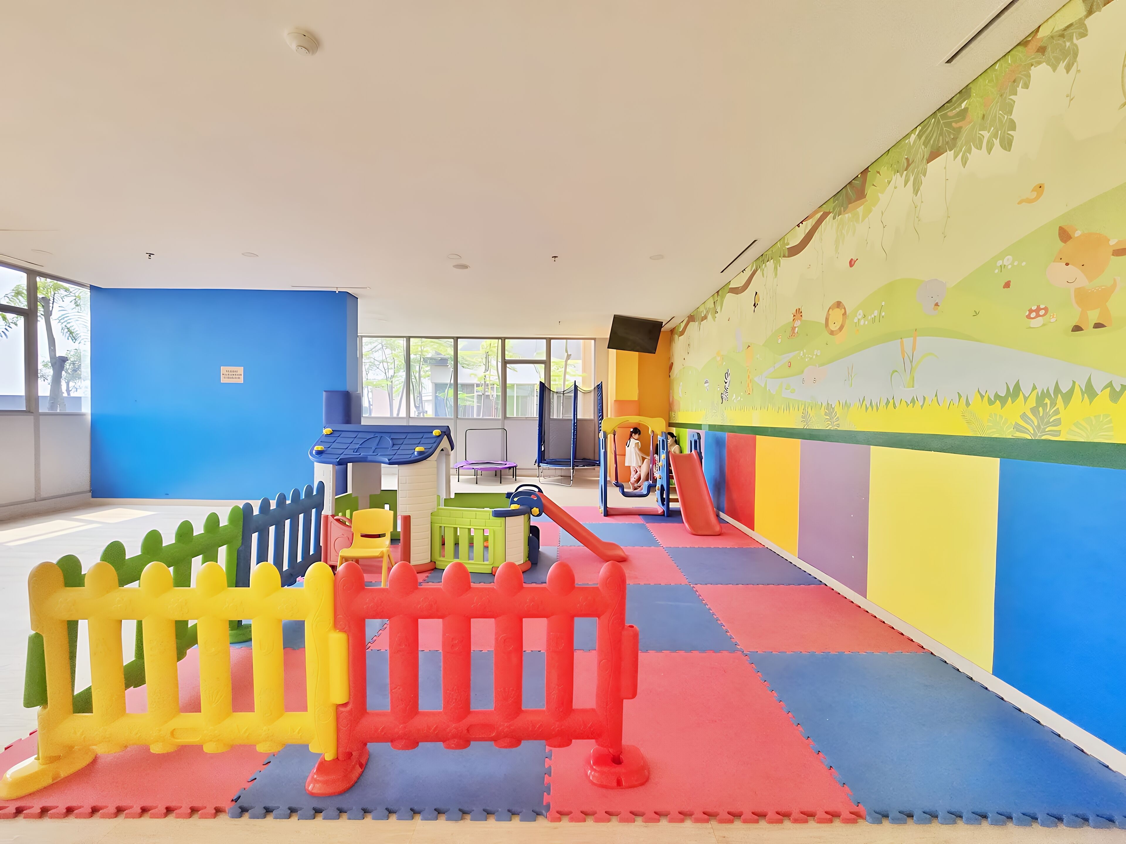 Ein Kinderspielbereich mit bunten Matten, Spielgeräten und einem Wandgemälde.