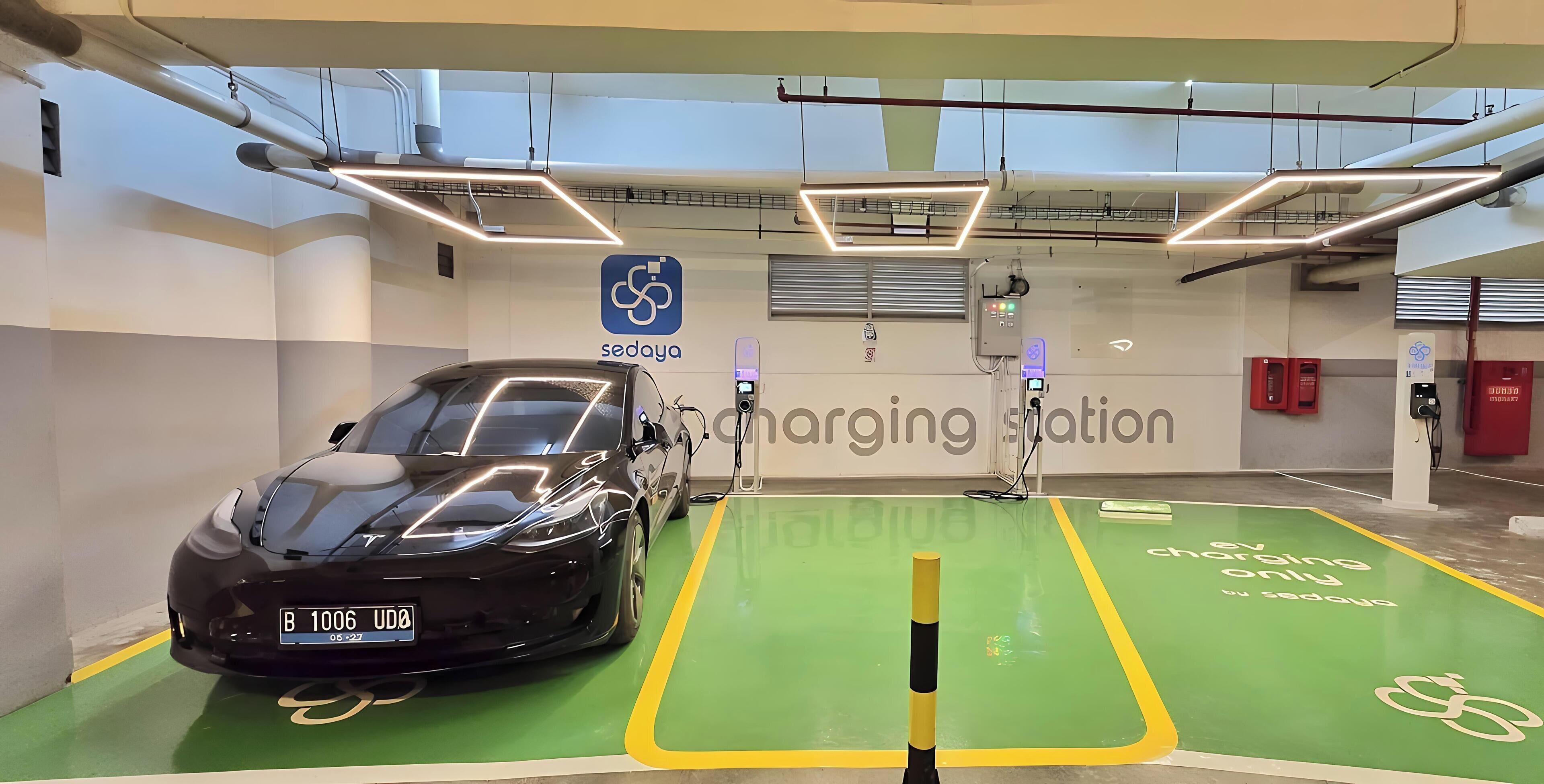 Una estación de carga para automóviles con piso verde, un auto negro y un letrero que dice 'sedoya'.