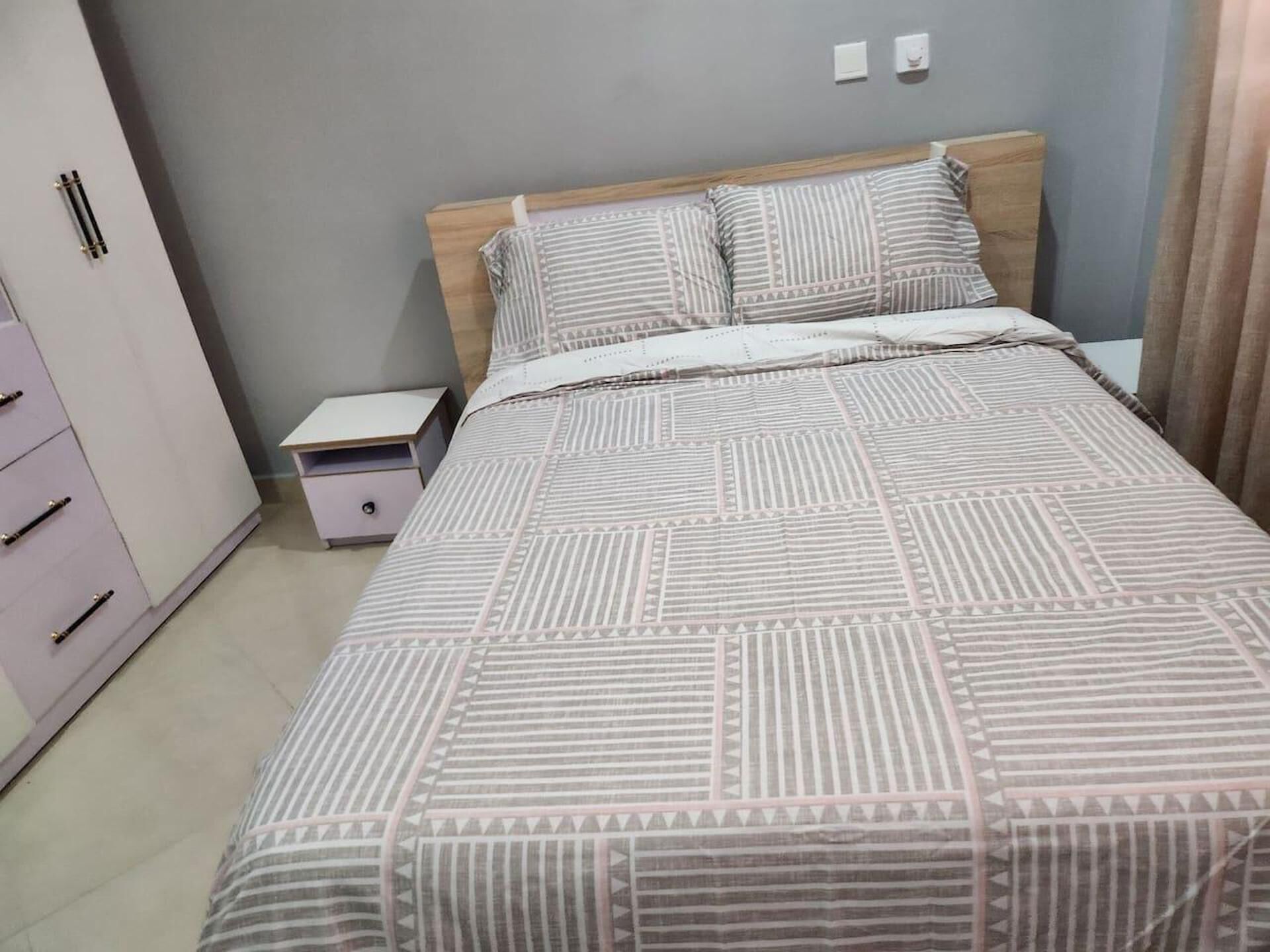 Ein ordentlich bezogenes Bett mit gestreifter Bettwäsche, ein hölzerner Kopfteil und ein kleiner Nachttisch mit Schublade.