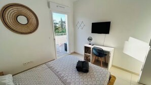 Une chambre avec un lit, un bureau, une télévision et un balcon.