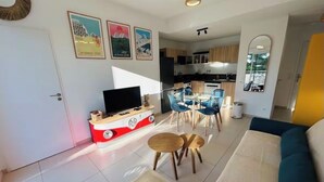 Un salon moderne comprenant un canapé, un téléviseur et un coin repas avec des chaises et une table.