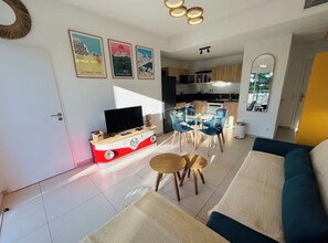 A modern living room with a sofa, a TV, and a dining area with chairs and a table. - T3 large terrace - parking WIFI - CLIM 5P (La Grande-Motte)