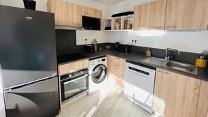 Une cuisine moderne avec un réfrigérateur noir, un lave-linge, un lave-vaisselle, des armoires en bois et un four à micro-ondes.
