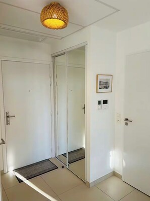 A hallway with a sliding door, a framed picture on the wall, and a textured ceiling light fixture. - T3 large terrace - parking WIFI - CLIM 5P (La Grande-Motte)
