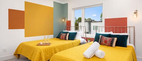 A hotel room with two beds, a ceiling fan, a window with a view, and a small table with bottles.