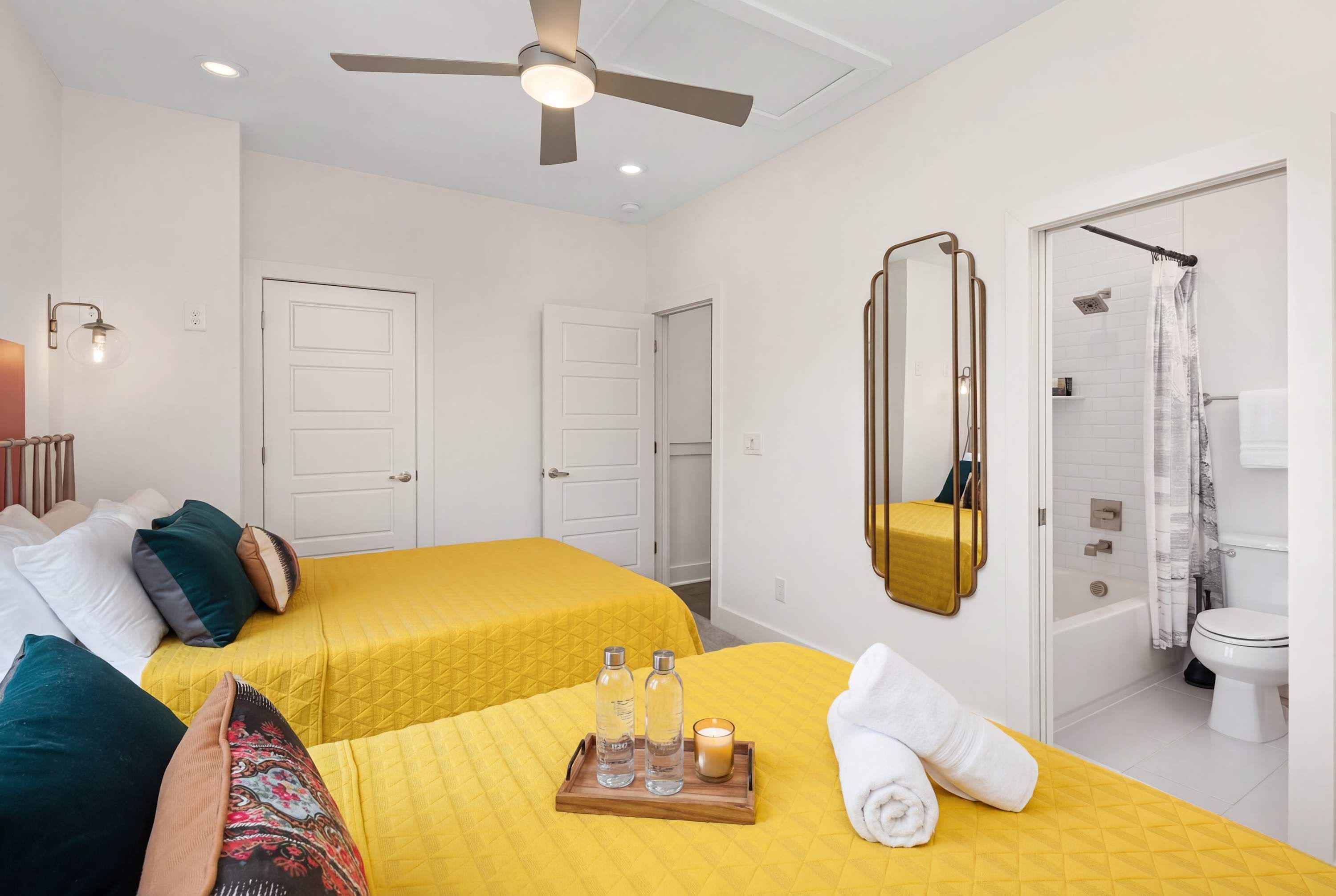 Une chambre d’hôtel avec deux lits, un ventilateur de plafond, un miroir et une salle de bain avec douche et toilettes.