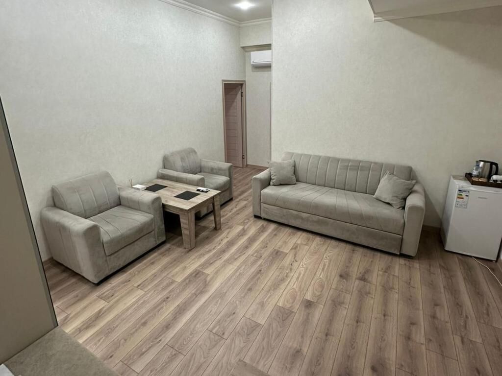 Uma sala de estar com sofá, duas poltronas, uma mesa de centro e uma geladeira.