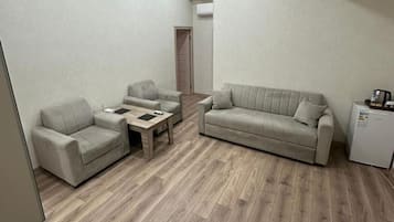 Uma sala de estar com sofá, duas poltronas, uma mesa de centro e uma geladeira.