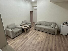 Una sala de estar con un sofá, dos sillones, una mesa de centro y un refrigerador.