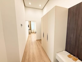 Um corredor com piso de madeira, parede branca e um guarda-roupa com painel escuro.