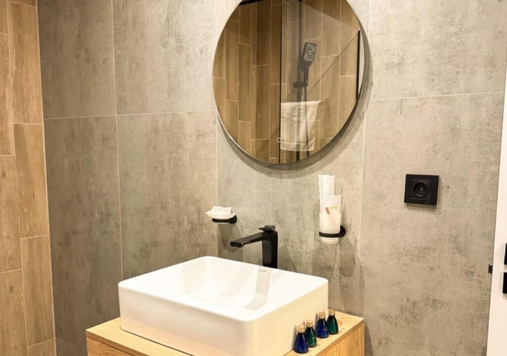 A bathroom with a white sink, a round mirror, and a towel rack.