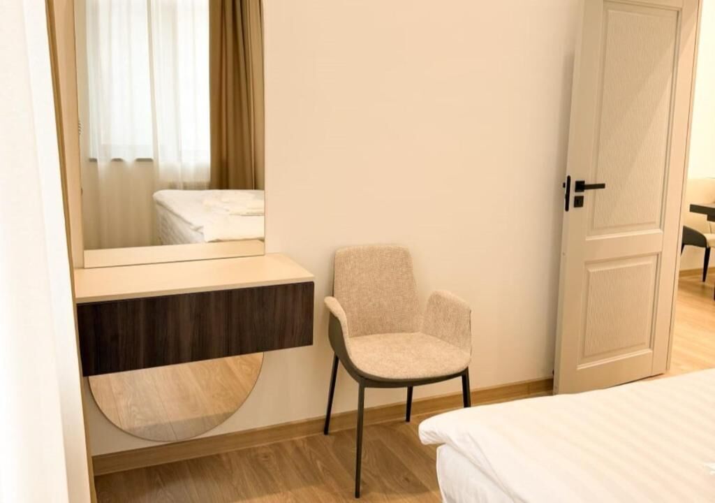 A hotel room with a bed, a chair, a vanity with a mirror, and a door.