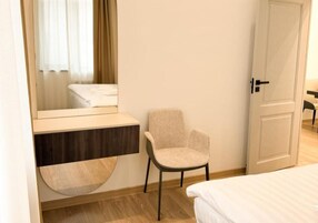 A hotel room with a bed, a chair, a vanity with a mirror, and a door.