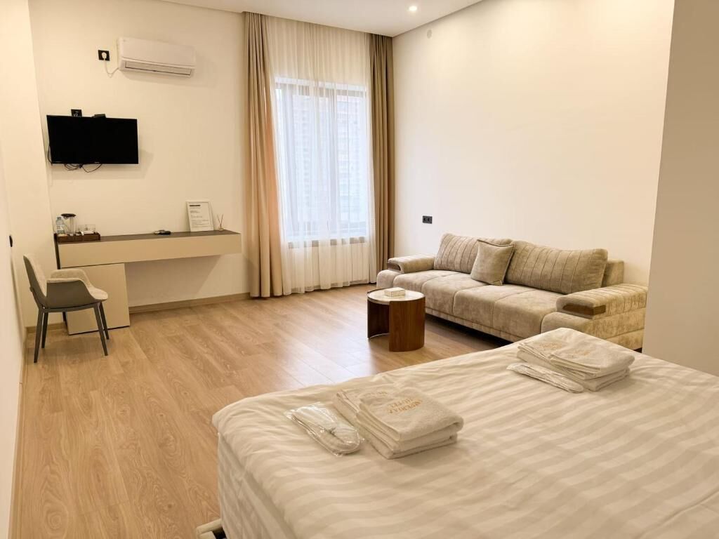 A hotel room with a bed, a sofa, a desk, and a TV.