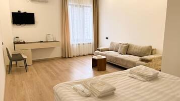 A hotel room with a bed, a sofa, a desk, and a TV.